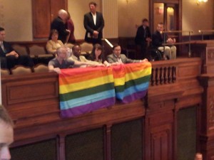Left-wing Chicago homosexual activist Andy Thayer of Gay Liberation Network (GLN) unfurls homosexualist "rainbow flag" in the gallery of the Illinois House yesterday. Photo: Dave Smith of Illinois Family Institute -- who reports that the Illinois "gay" lobby is still a few votes shy to pass homosexuality-based "marriage" before the session ends Friday, May 31..